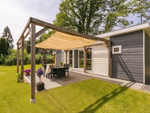 A covered patio with a table and chairs, a pergola, and a house with large windows.