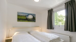 Una habitación de hotel con cama, ventana con cortinas, radiador y un cuadro en la pared.