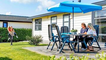 Un espace patio avec des sièges d’extérieur, un parasol bleu et une maison en arrière-plan.