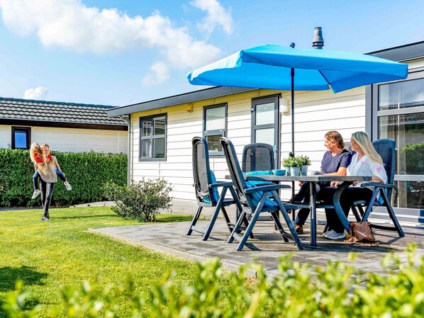 Eine Terrasse mit Sitzgelegenheiten im Freien, einem blauen Sonnenschirm und einem Haus im Hintergrund.