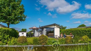Ein modernes Haus mit einem großen Glasfenster, einer kleinen angebauten Garage und einem Teich im Vordergrund.