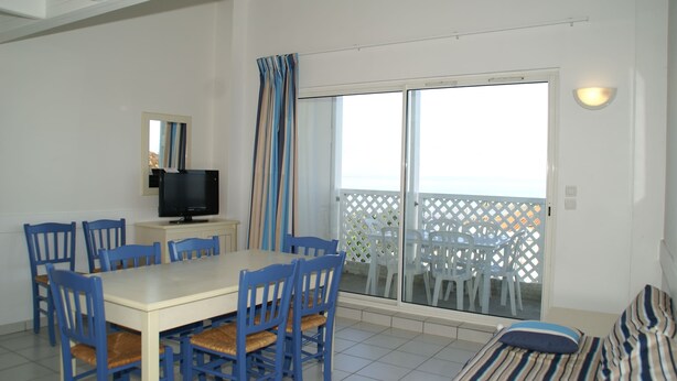 A room with a dining table, chairs, a TV, a sofa, and a balcony with a white fence. - Coastal Getaway With Pool (Fouras)