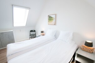Habitación individual con una ventana, una silla, una mesita de noche con lámpara y un cuadro en la pared.