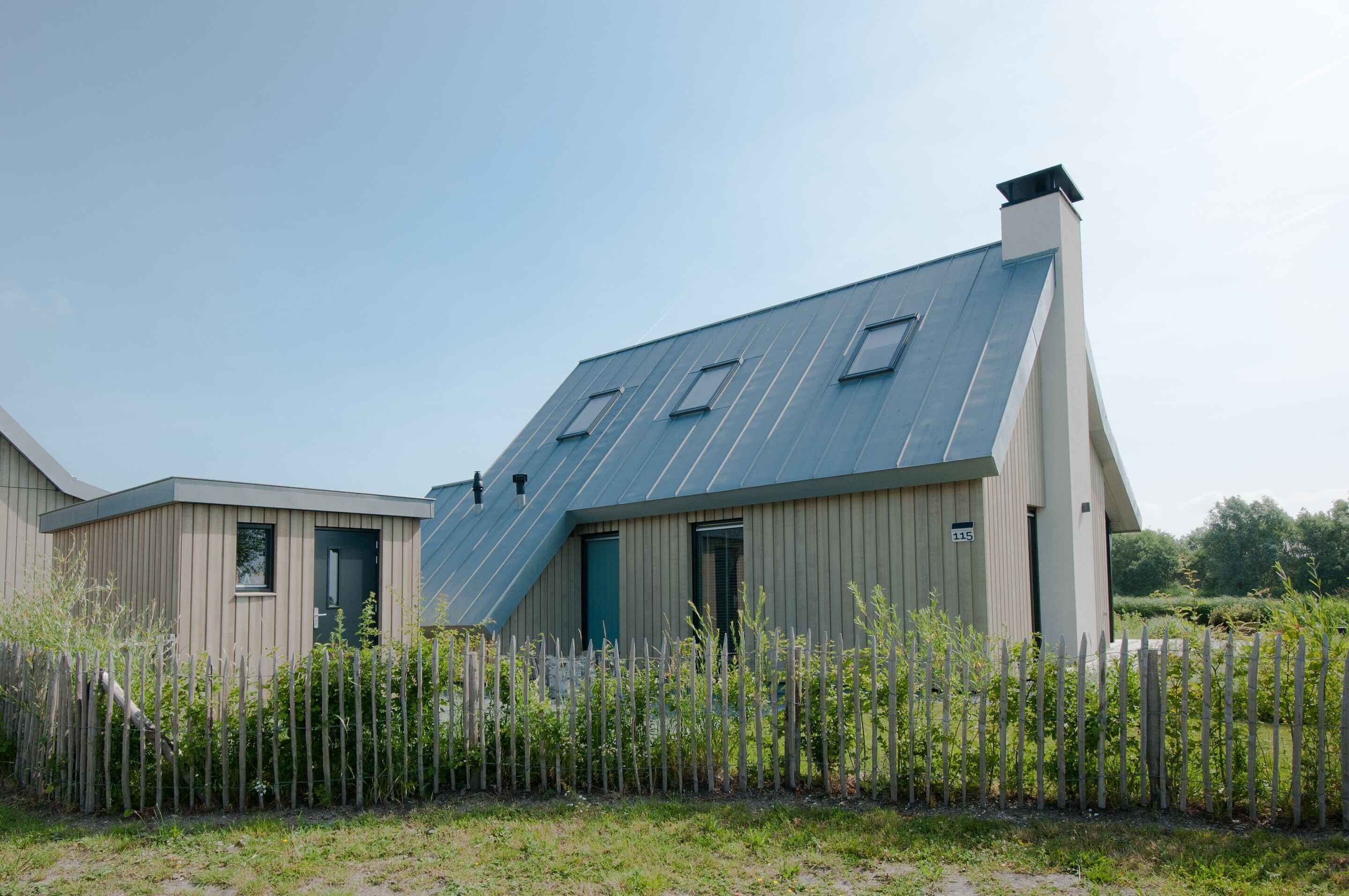 A modern building with a sloped roof, a fenced area in front, and a clear sky.