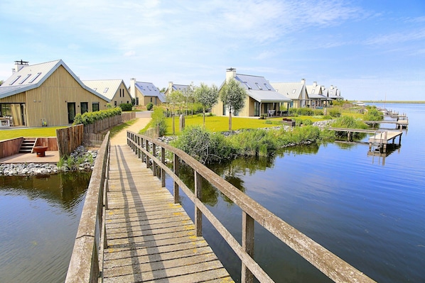 A wooden dock leading to a row of buildings with sloped roofs, a calm water body, and a clear sky.