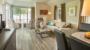 Un salon moderne avec un canapé, une table basse et des fauteuils. On y trouve un téléviseur posé sur un meuble, ainsi qu’une fenêtre avec des rideaux.