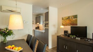 Une cuisine moderne avec des meubles gris, une table à manger avec des chaises, un téléviseur et un tableau accroché au mur.