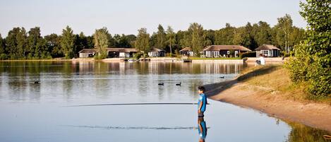 Un lac paisible, bordé de maisons, où une personne est en train de pêcher.