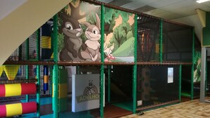 Un espace de jeux pour enfants avec une structure d’escalade, un toboggan et une fresque murale représentant des personnages de dessins animés.