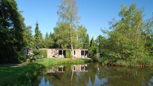 Un chalet au bord du lac, dont l’image se reflète dans l’eau, entouré d’arbres.