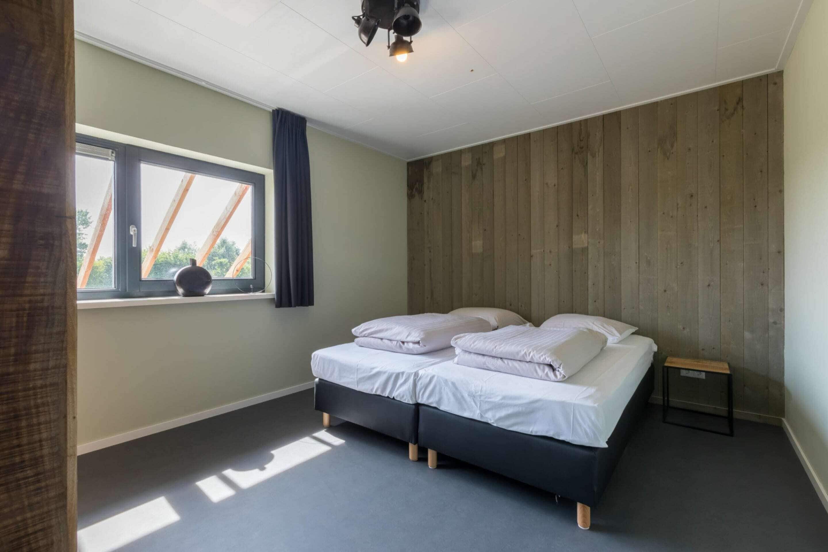 Ein Zimmer mit Bett, Fenster, Deckenlampe und einer Holzwand.