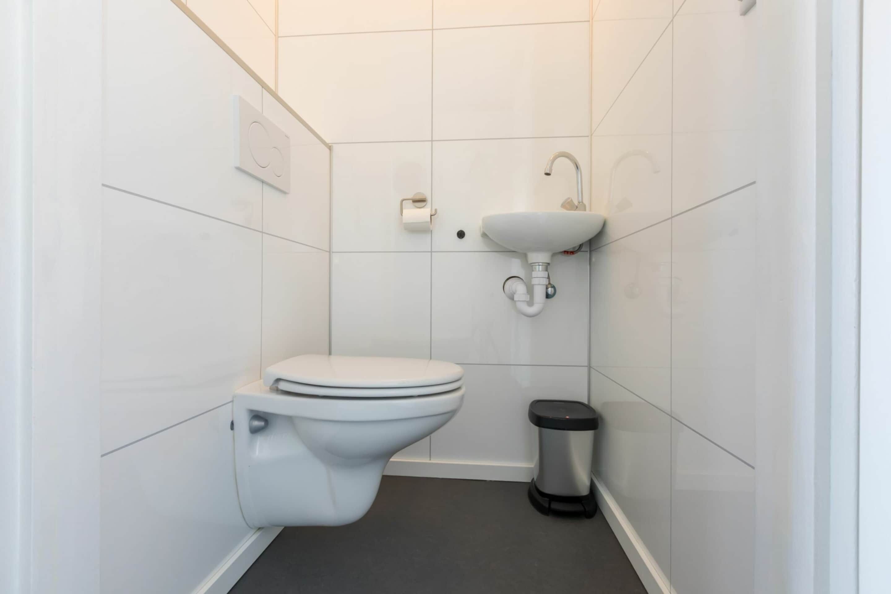 Une petite salle de bain moderne, équipée de toilettes, d’un lavabo et d’une poubelle.