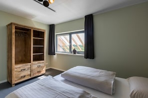 Ein Schlafzimmer mit zwei Betten, einem Holzschrank, einem Fenster mit Vorhängen und Blick ins Grüne.