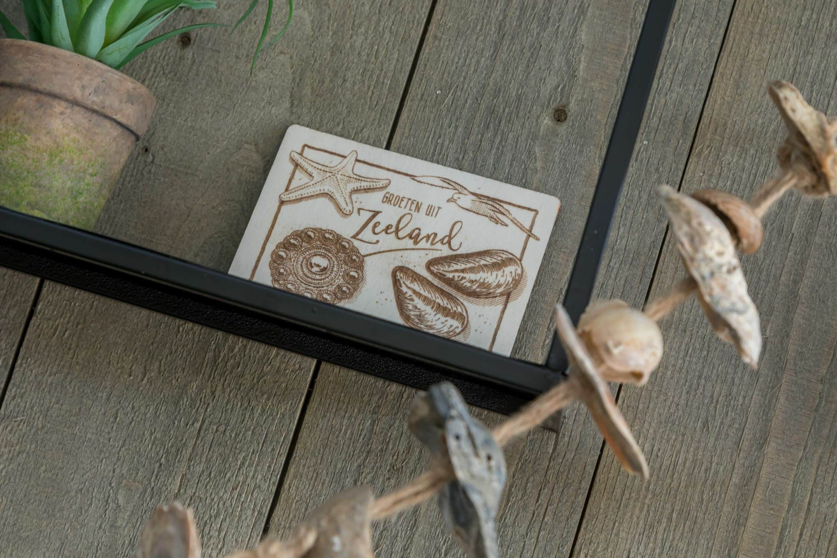 A framed card with illustrations of sea creatures and the text 'Grotten mit Zeeland' on a wooden surface.