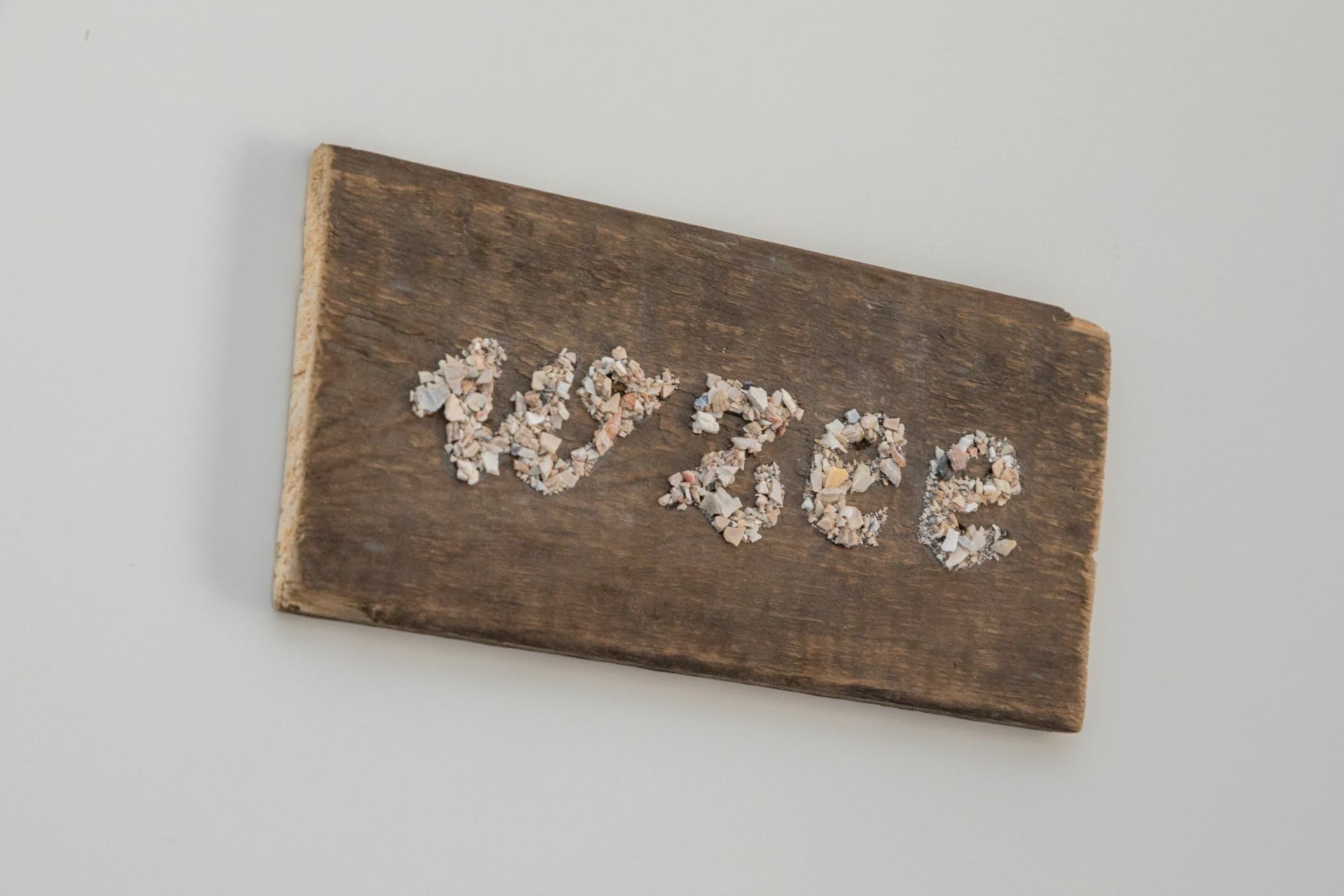 Eine rechteckige Holzplakette, auf der das Wort 'LOVE' in weißen Kieselsteinen geschrieben ist.