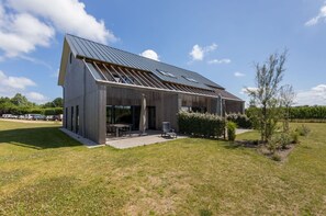 A modern house with a sloped roof, large windows, and a patio area with outdoor furniture. - Holiday Home in Vrouwenpolder Near Beach (Vrouwenpolder)