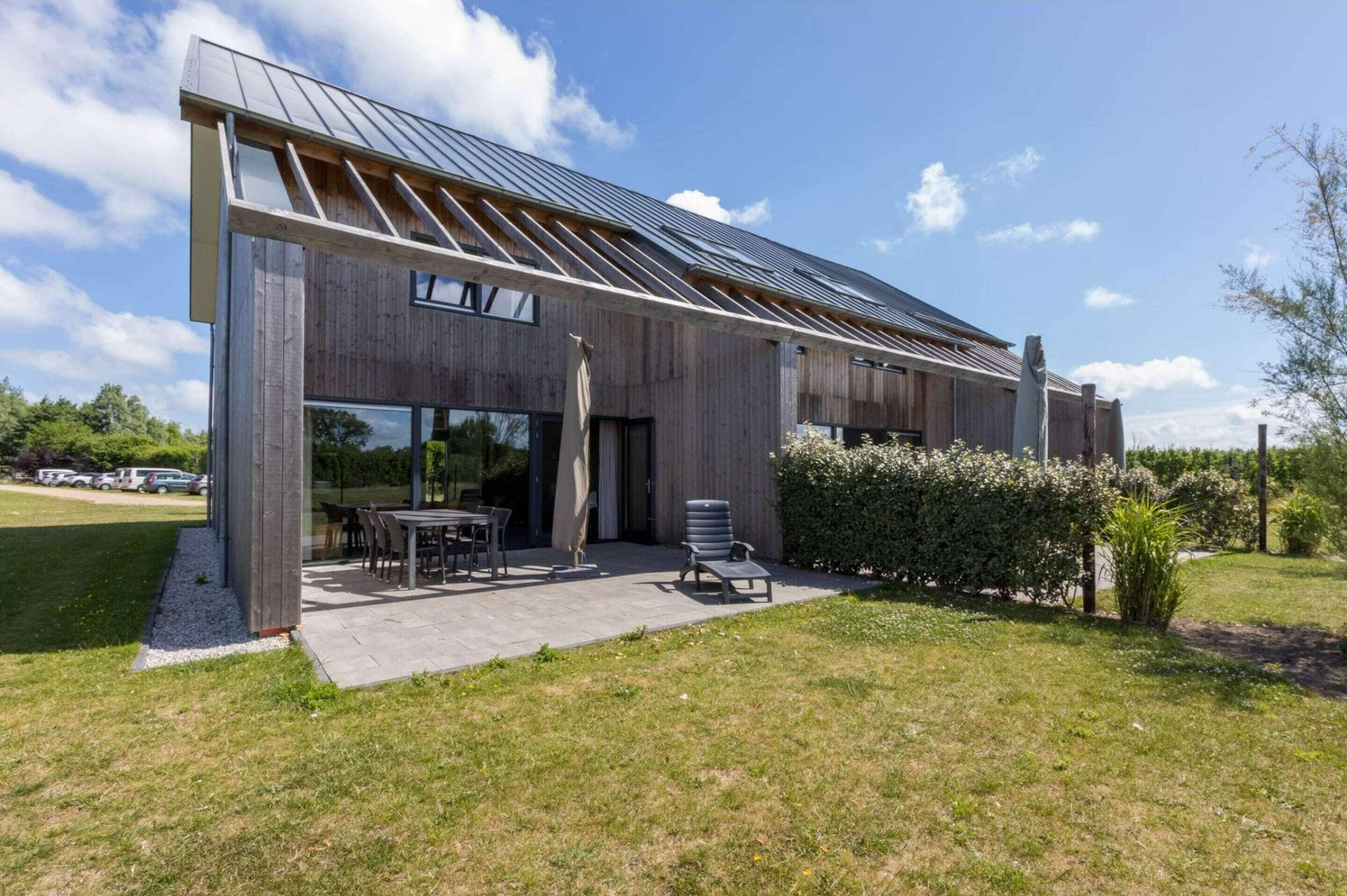 Ein modernes Gebäude mit geneigtem Dach, großen Fenstern und einer Terrasse mit Gartenmöbeln.