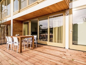 Eine Holzterrasse mit Tisch und Stühlen, eine Schiebetür und Blick auf den Garten.