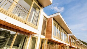 Un immeuble résidentiel moderne doté de nombreux balcons, de grandes fenêtres et d’une clôture en bois.