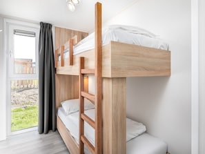 A bunk bed with a ladder, white bedding, and a view of a fenced outdoor area through a window with curtains.