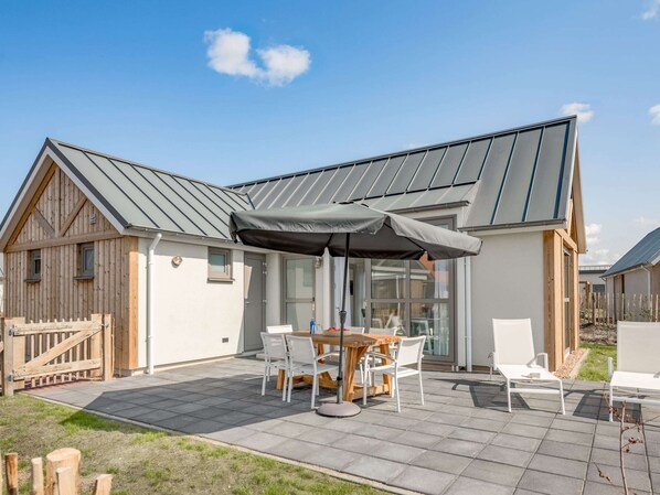 A modern house with a patio area featuring a table and chairs, a covered seating area, and a metal roof.