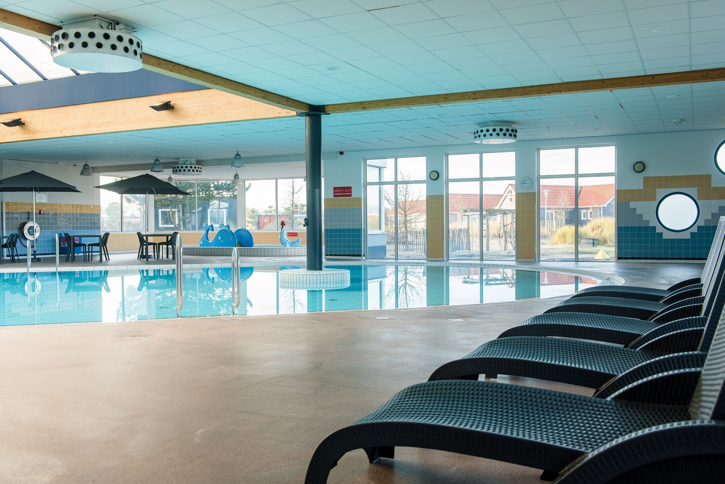 Un área de piscina interior con sillones de descanso, mesa de billar y toldo.