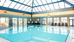 Una piscina interior con techo de tragaluces, vista despejada al exterior y zona de estar.