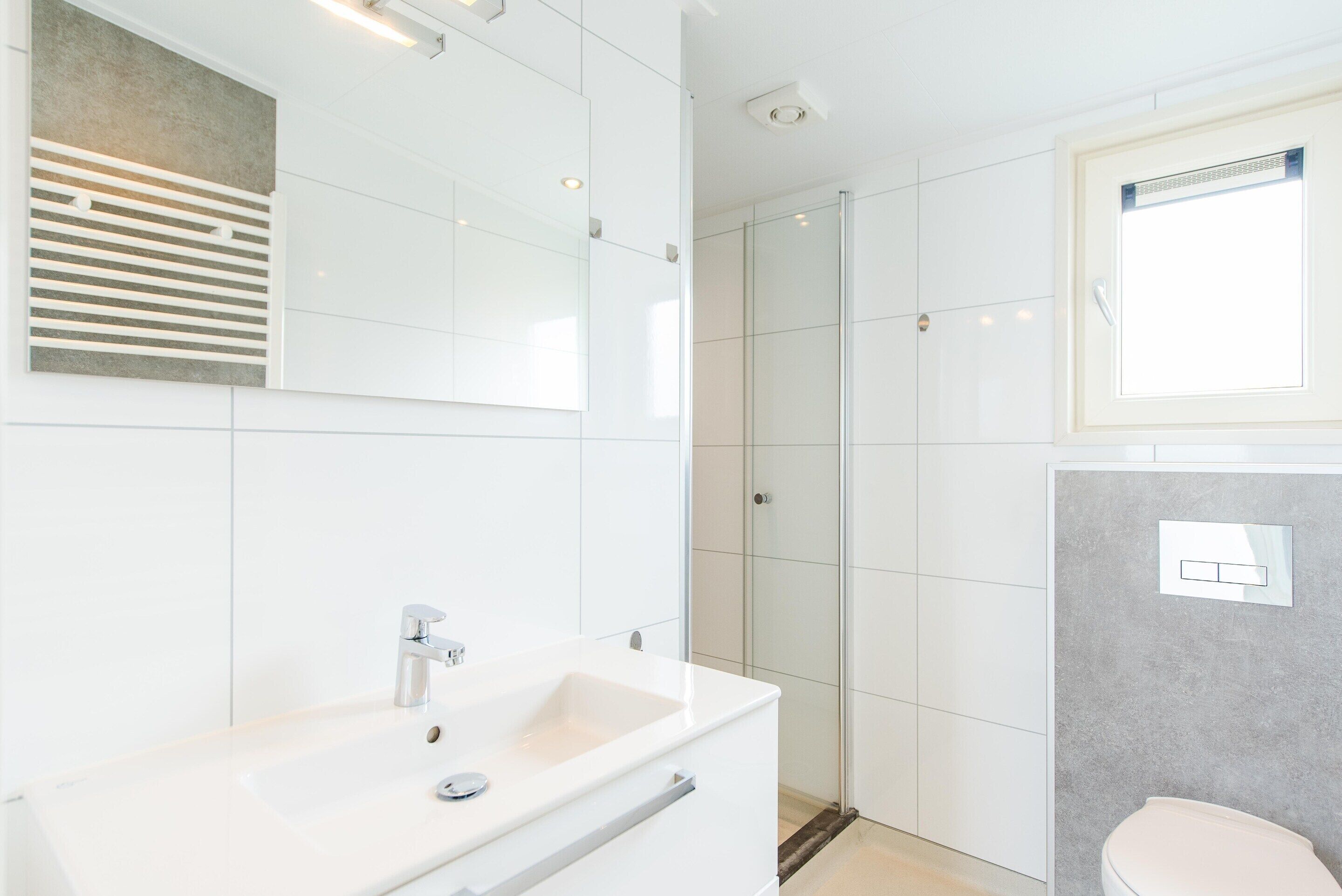 Ein modernes Badezimmer mit einem weißen Waschbecken, einer Duschkabine aus Glas und einer Toilette.