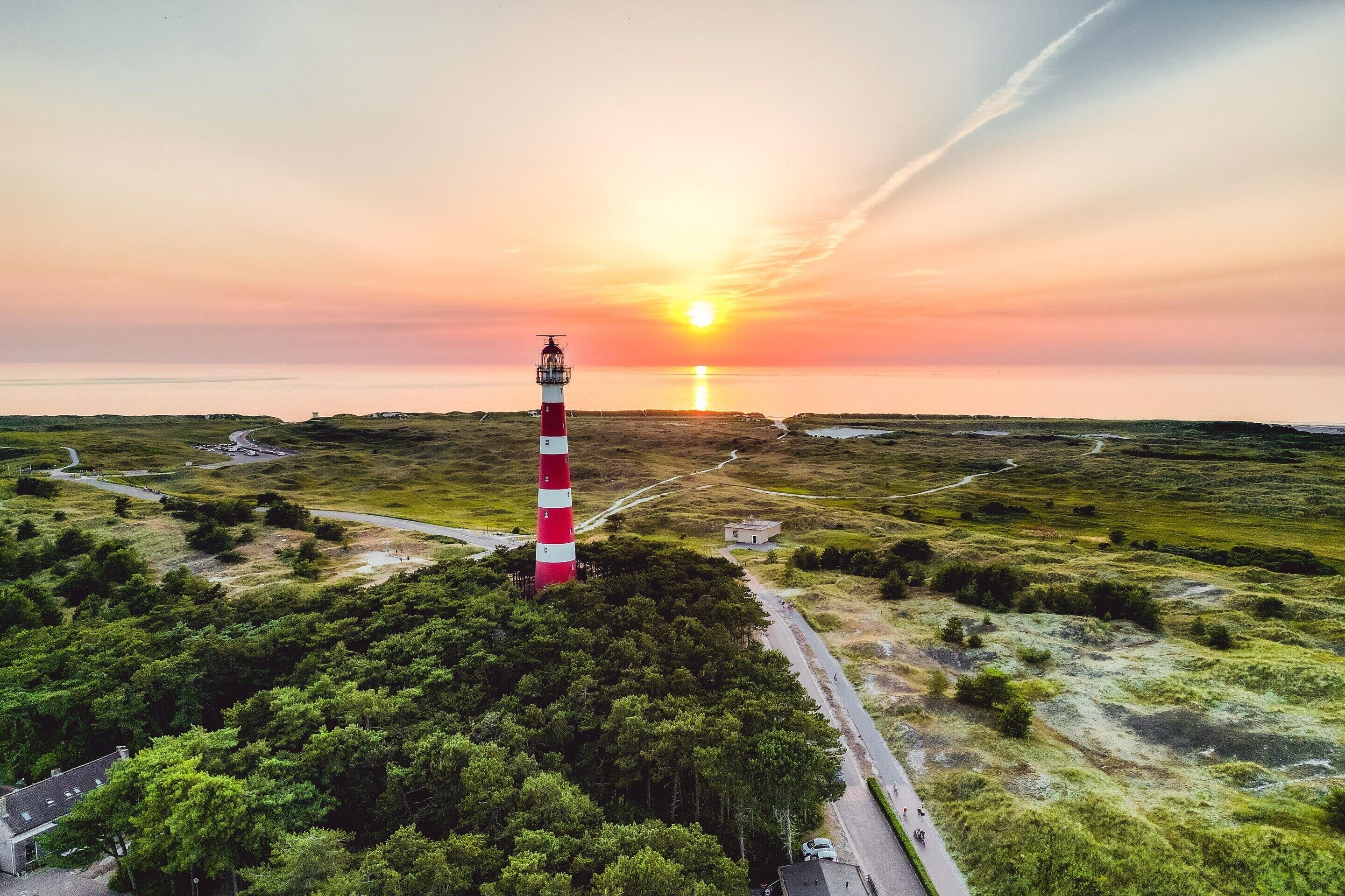 Un phare se dresse sur une colline herbeuse, et une route y mène.