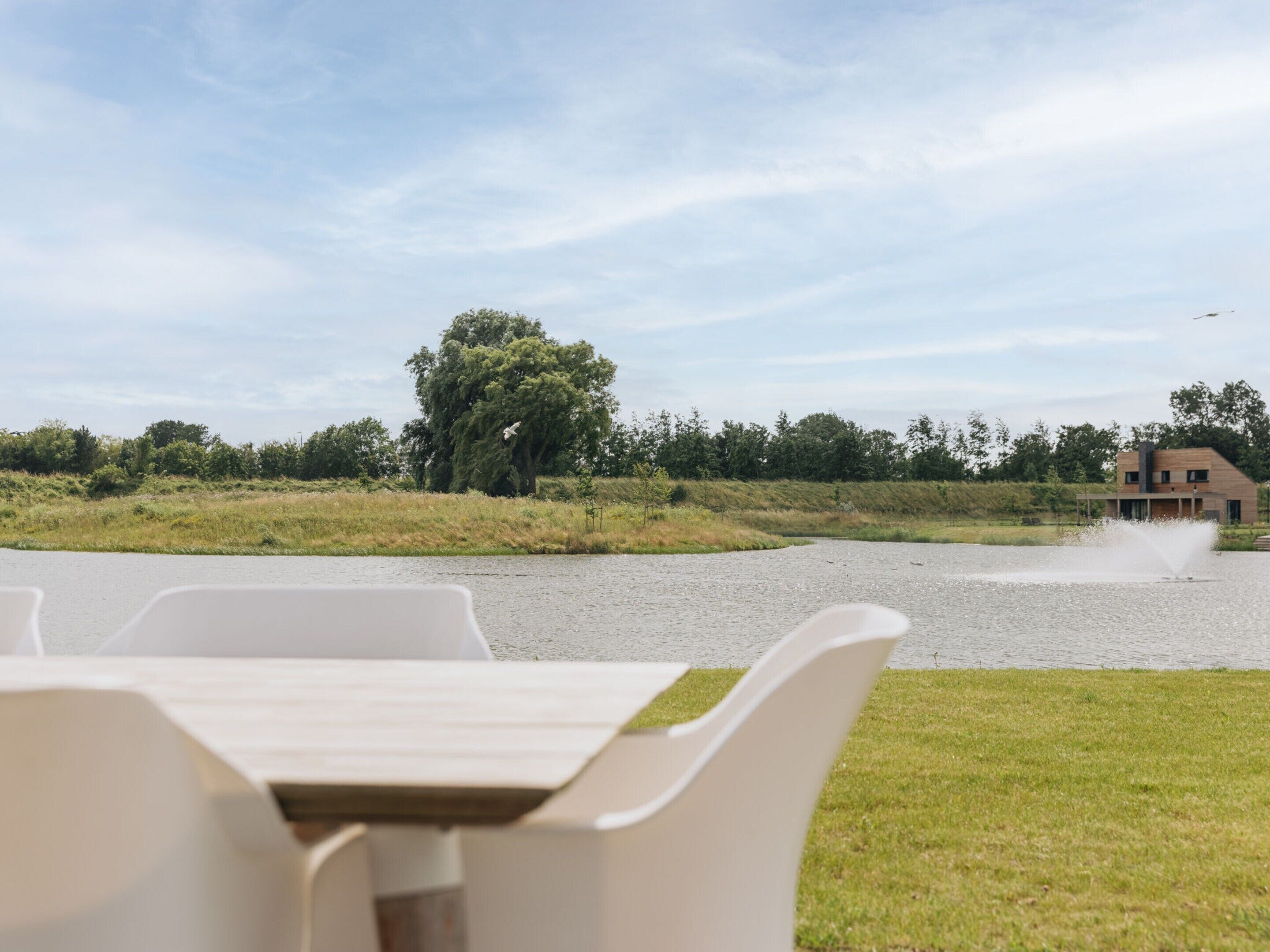 A view of a modern outdoor seating area with a table and chairs, a water feature, and a building in the background.