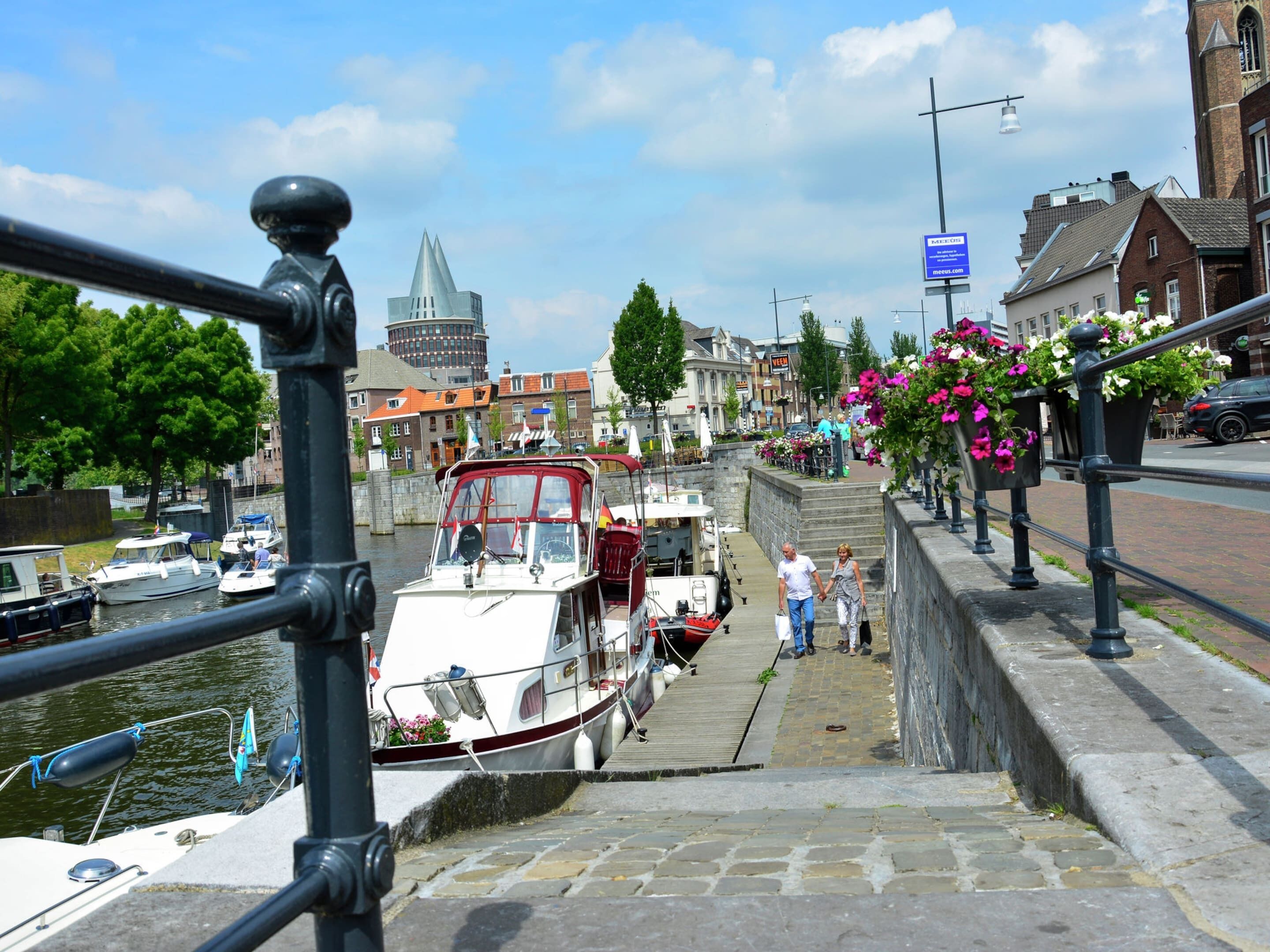 Un canal bordé de bateaux amarrés, un escalier en pierre menant à un pont et des bâtiments en arrière-plan.