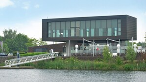 A modern building with a flat roof, large windows, and a bridge leading to it. - Villa With Lake Views (Heel)