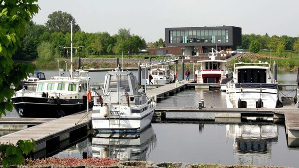 A marina with several boats docked, a modern building in the background, and a calm water body. - Villa With Lake Views (Heel)