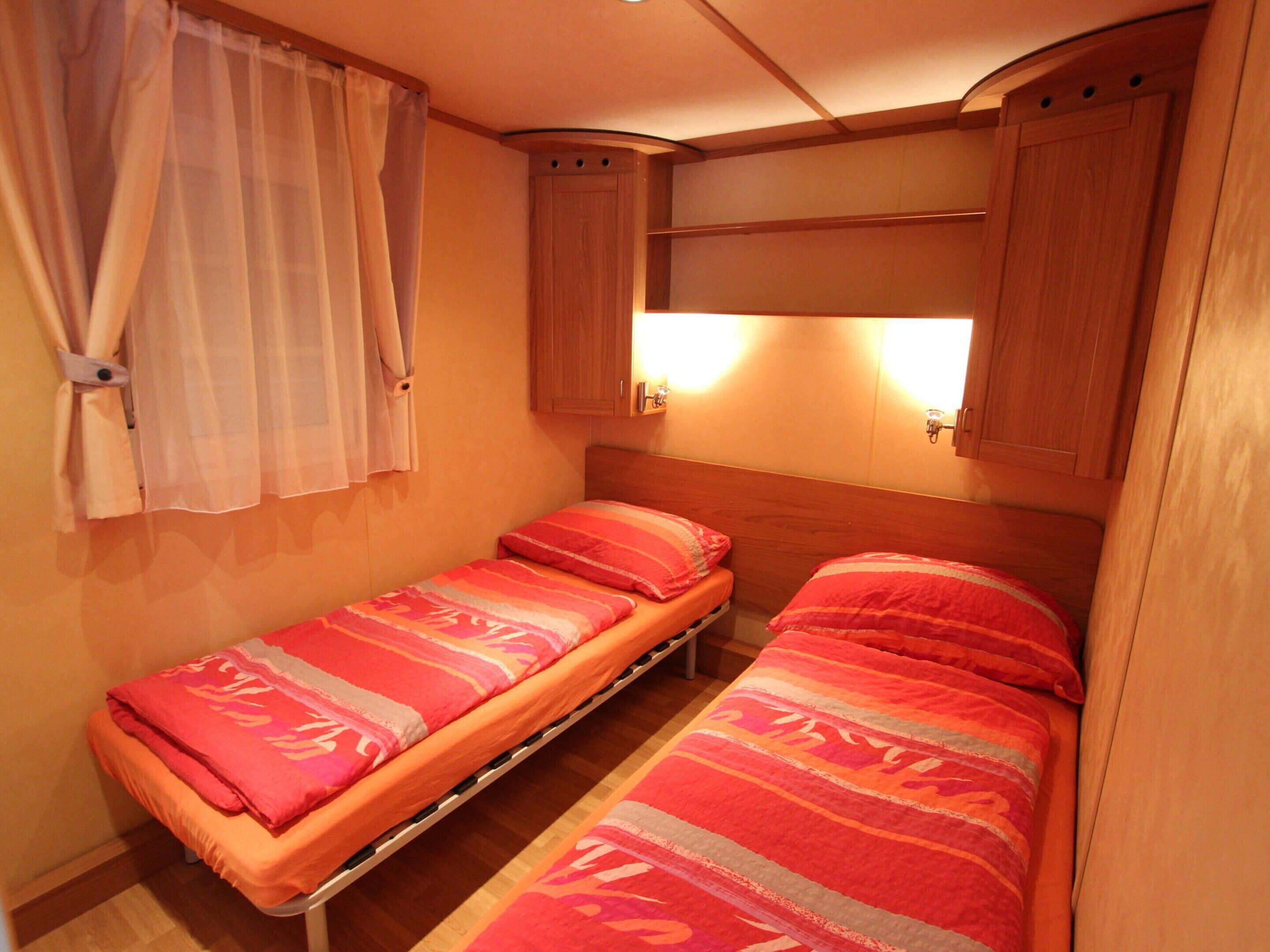 A small, cozy bedroom with two single beds, wooden headboards, and a window with curtains.