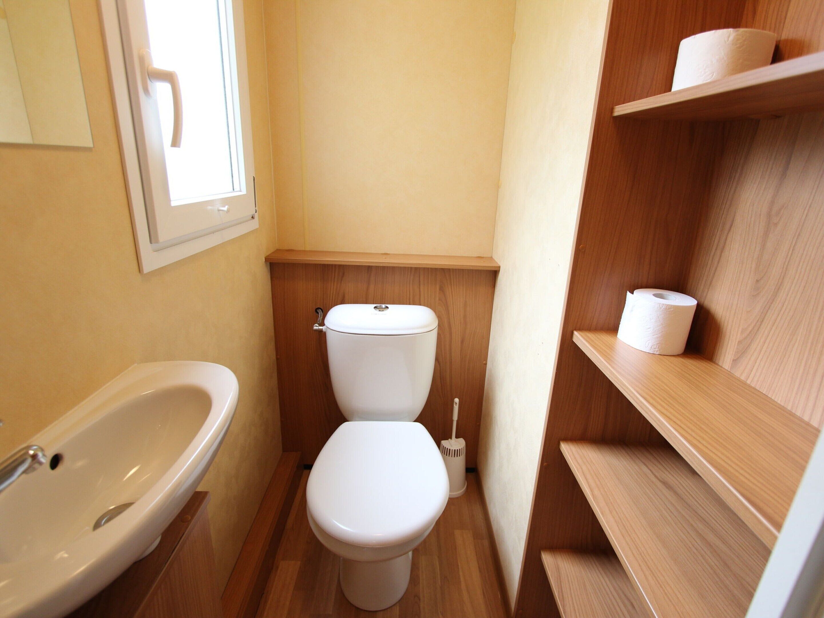 Une petite salle de bain comprenant des toilettes, un lavabo et une étagère avec du papier toilette.