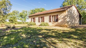 A single-story building with a tiled roof and wooden shutters, surrounded by a grassy lawn and trees. - Holiday Home With Swimming Pool (Salignac-Eyvignes)