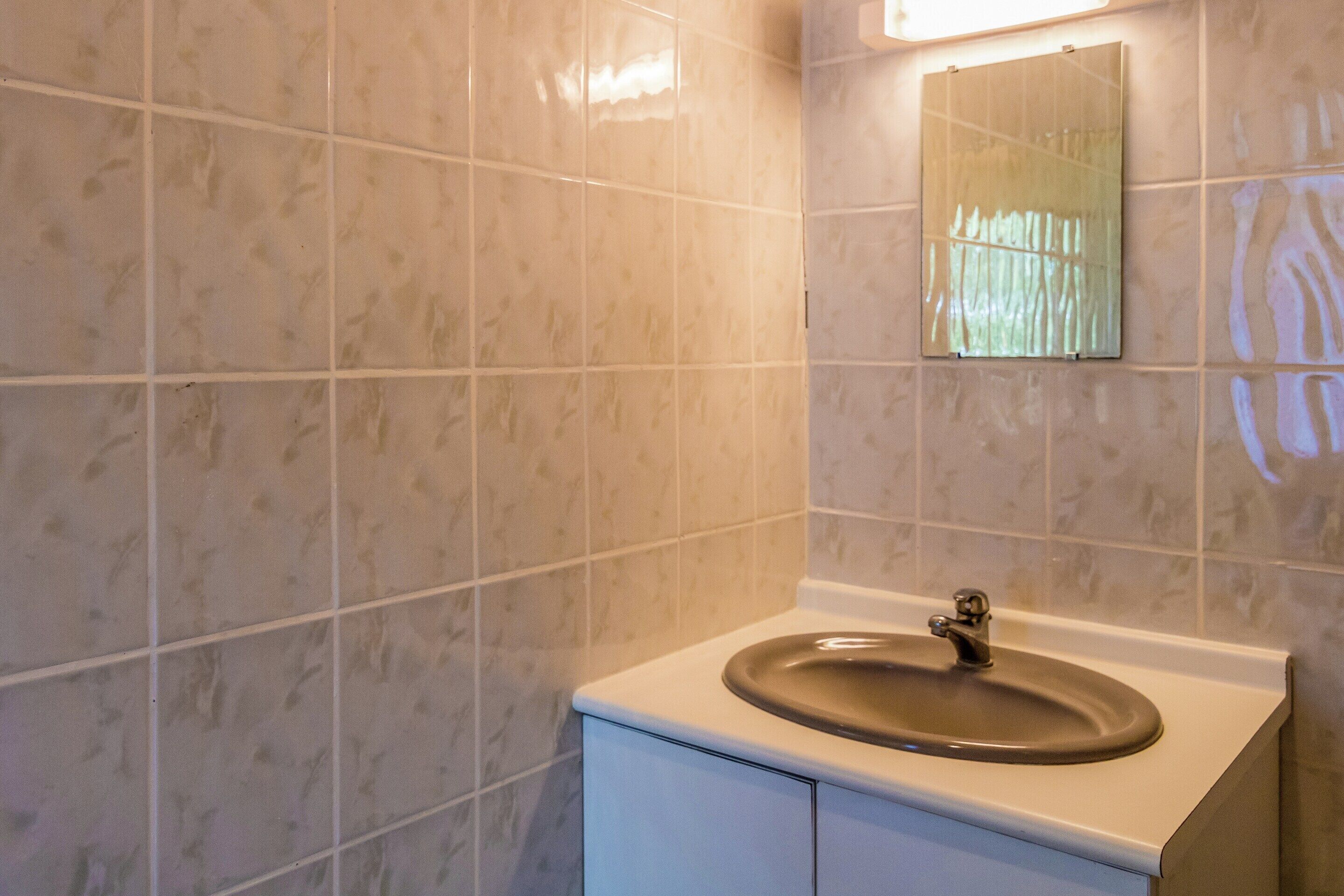 A bathroom with a sink, mirror, and tiled walls.