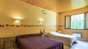 A room with two beds, a nightstand, a lamp, and a window with a view of trees. - Holiday Home With Swimming Pool (Salignac-Eyvignes)