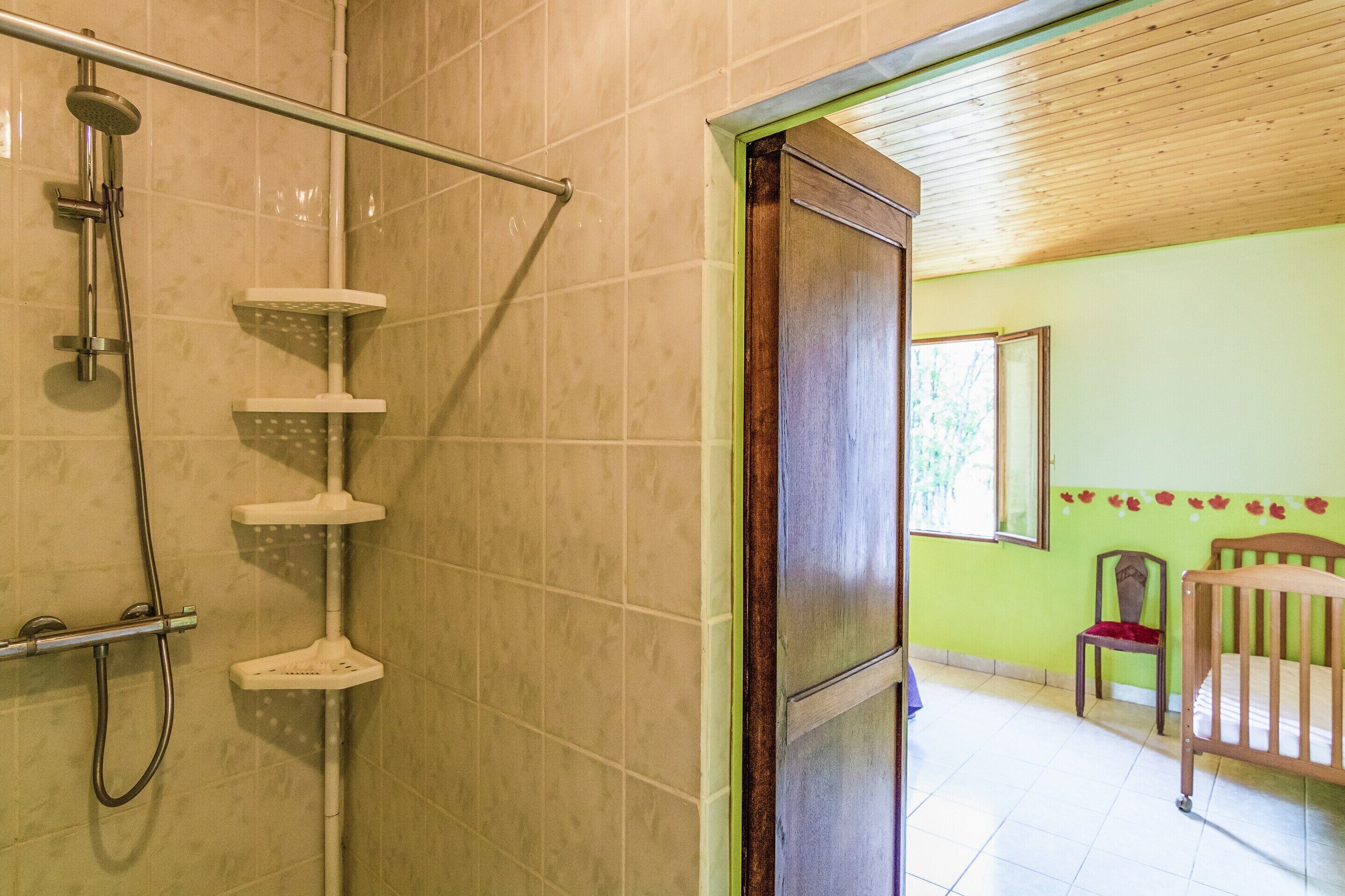 Un baño con ducha, una puerta de madera, una silla y una cama.