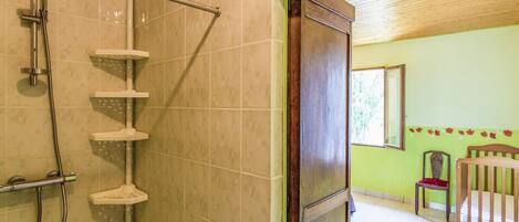 Un baño con ducha, una puerta de madera, una silla y una cama.
