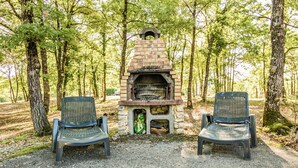 A brick outdoor oven with two chairs in a forested area. - Holiday Home With Swimming Pool (Salignac-Eyvignes)