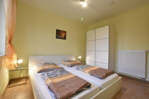 A double bed with patterned bedding, a bedside table with a lamp, a wall-mounted radiator, and a framed picture on the wall.