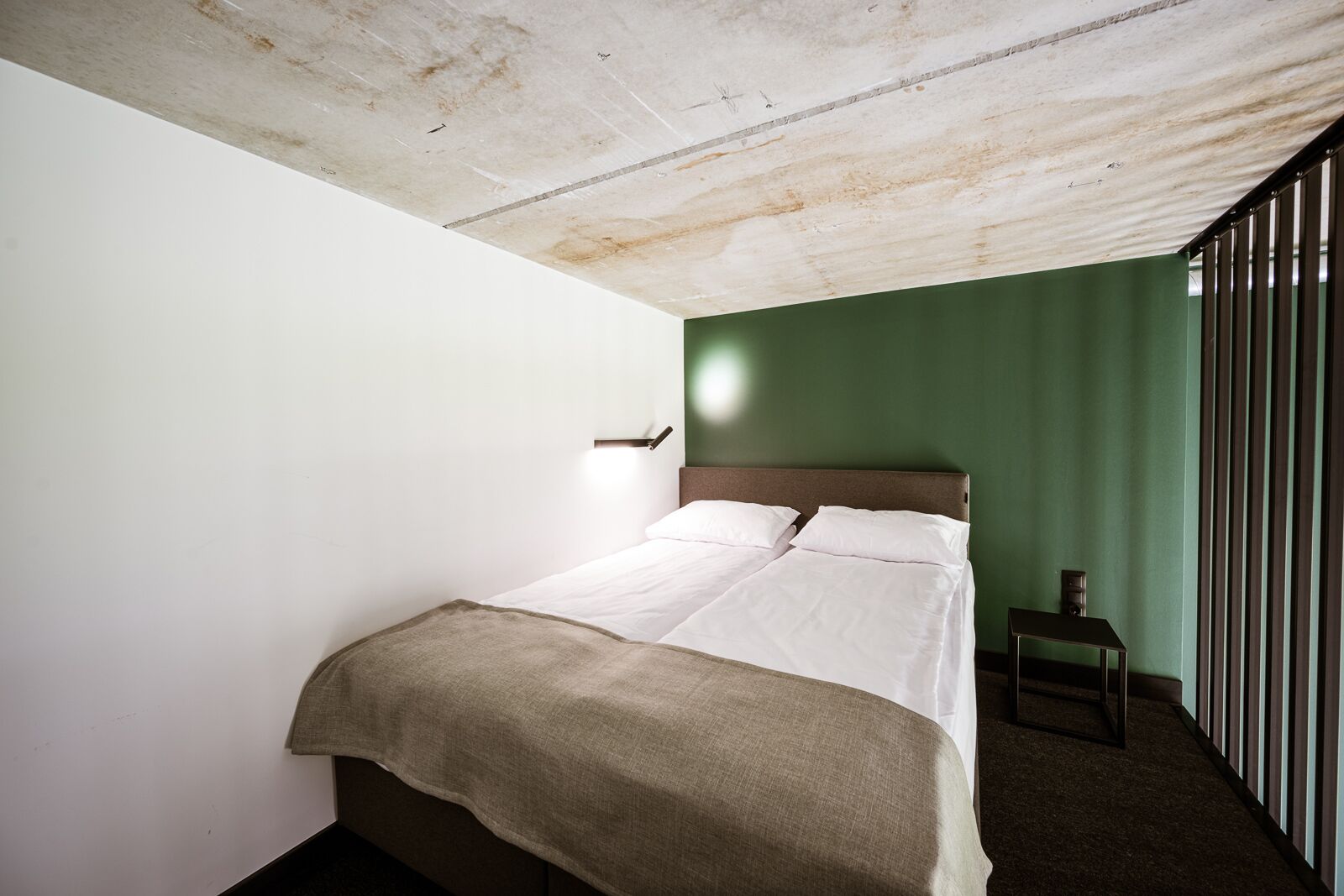 Una cama individual con cabecera de madera en una habitación con paredes verdes y techo blanco.