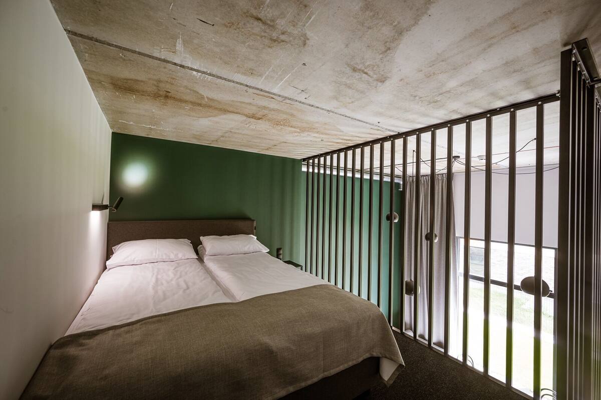 Una habitación con cama, una ventana con rejas y una pared verde.
