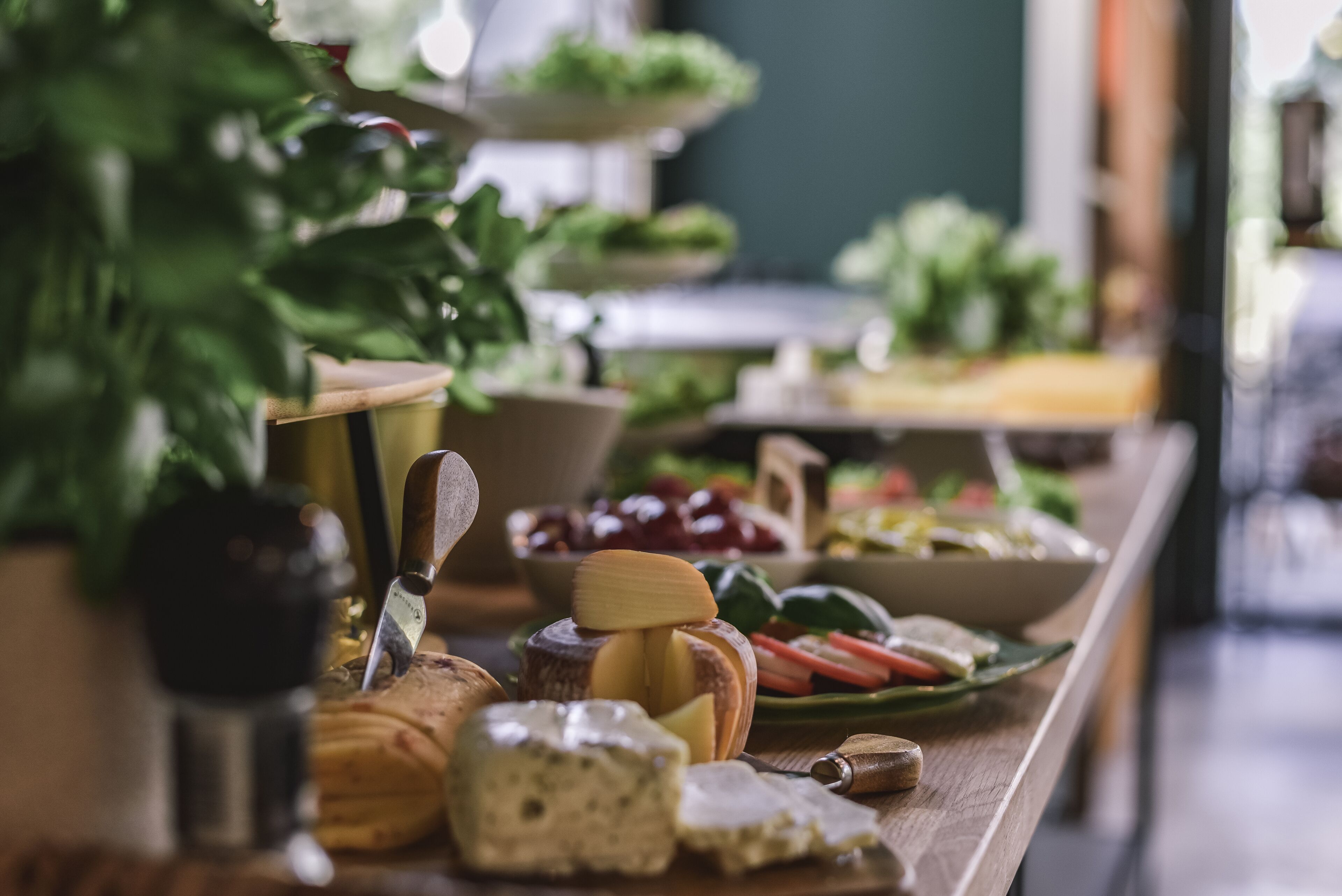 Una mesa de buffet con diversos alimentos, entre ellos queso, pan y verduras.