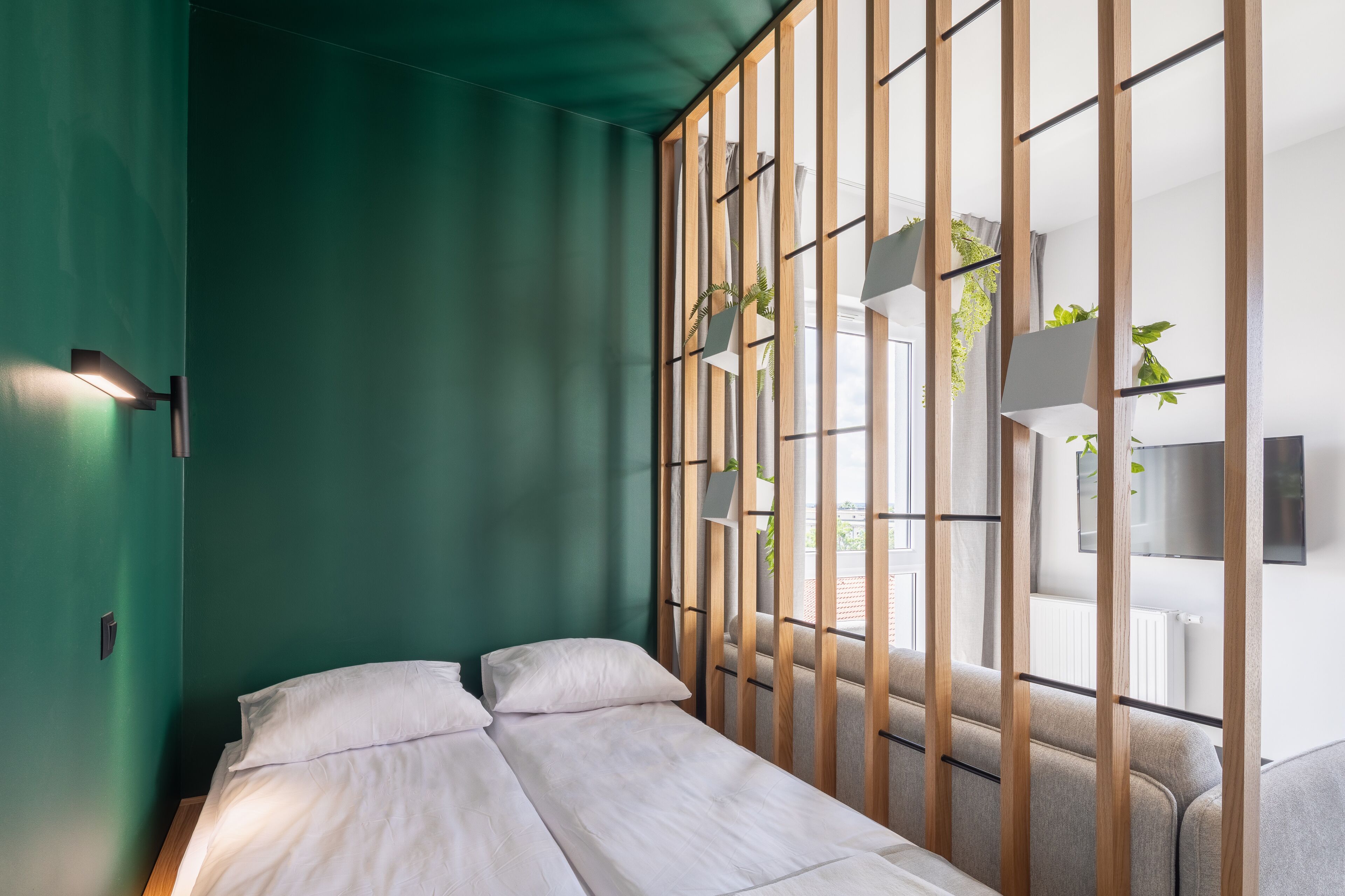 A room with a bed, a green wall, and a window with a view of the outside.