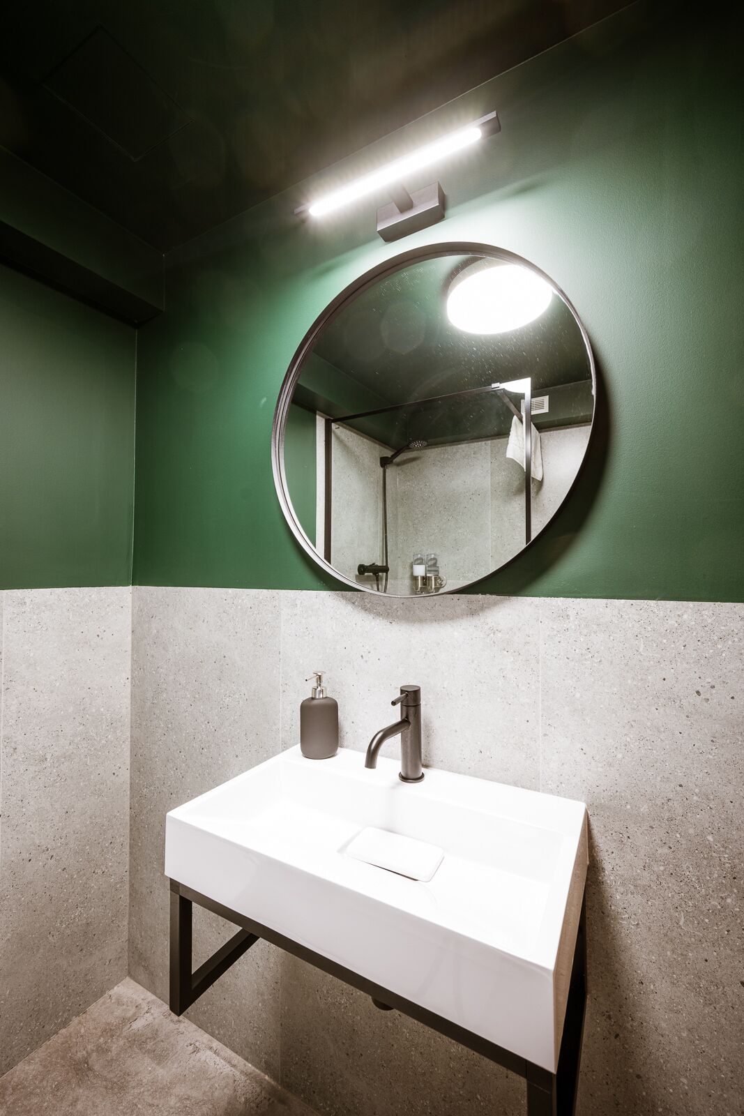 A bathroom with a white sink, a round mirror, and green walls.