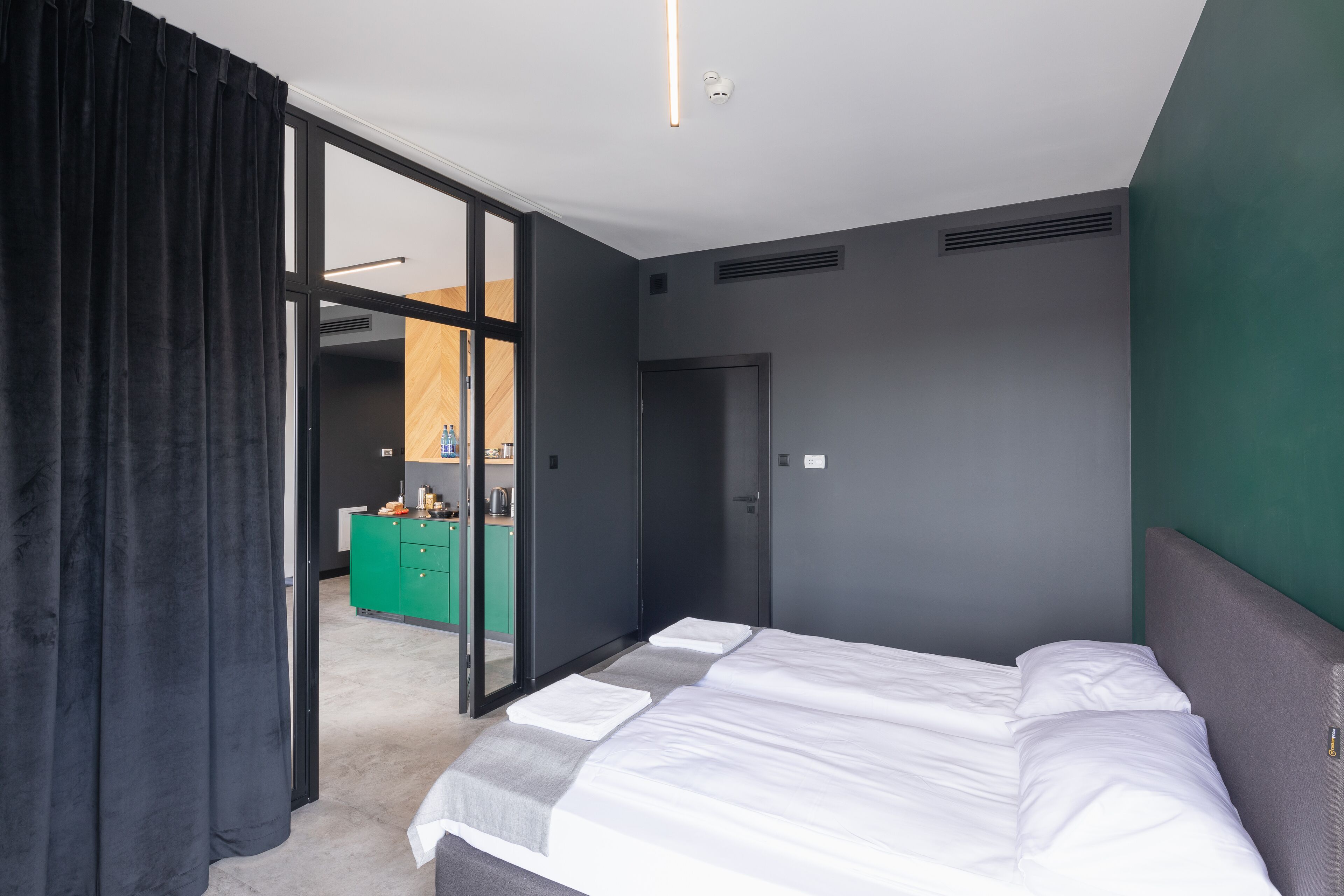 Ein modernes Hotelzimmer mit einem großen Bett, einer grünen Kommode und einer Schiebetür zu einem Badezimmer.