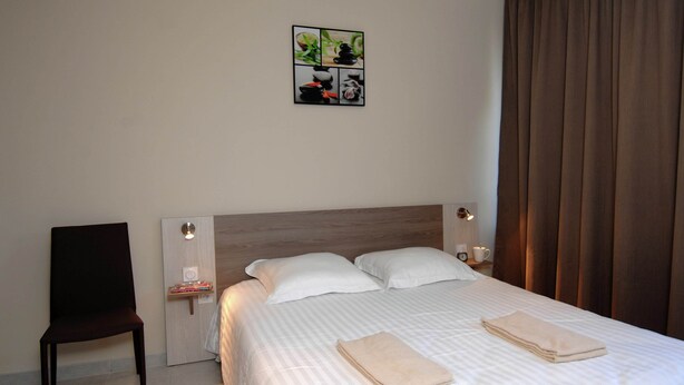 A hotel room with a bed, two pillows, a chair, a bedside table with a lamp, and a wall art piece. - Cap D'agde Retreat w/ Terrace (Agde)