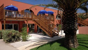 A hotel with a wooden balcony, blue umbrellas, and a palm tree. - Cap D'agde Retreat w/ Terrace (Agde)